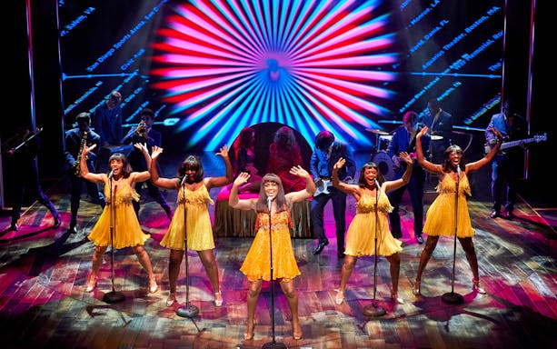 Performers in yellow dresses singing on stage during TINA: The Tina Turner Musical.
