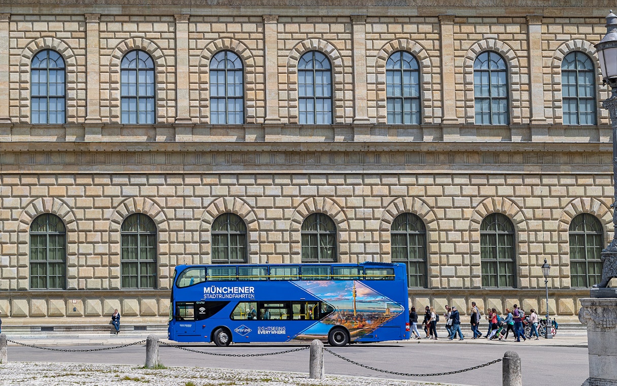 Blue double-decker tour bus in front of Munich's historic building on Hop-On/Hop-Off Express Tour.
