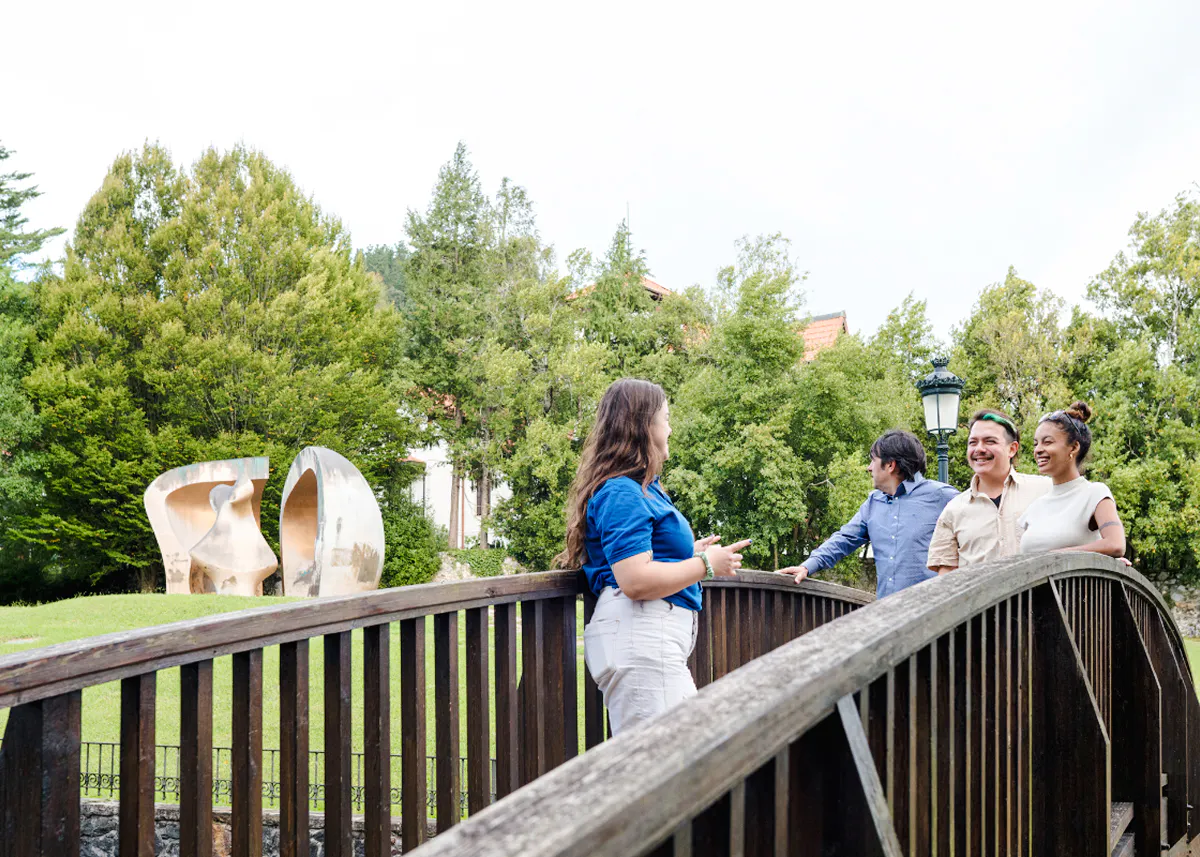 Visitors on a wooden bridge near a sculpture in San Sebastian park.