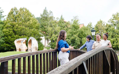 Visitors on a wooden bridge near a sculpture in San Sebastian park.