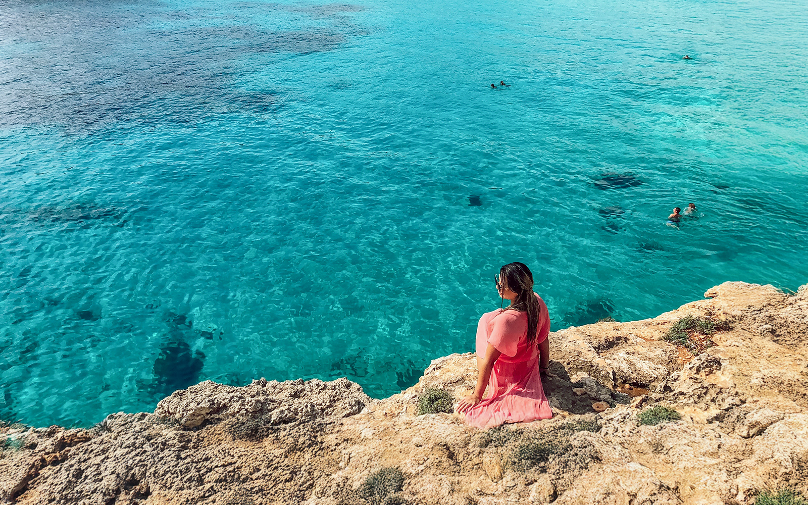 Tourist sitting on rocky shore overlooking Blue Lagoon, Malta.
