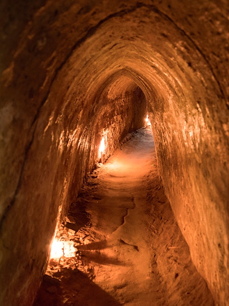 Narrow passage inside Cu Chi Tunnels, Vietnam, dimly lit with warm lights.