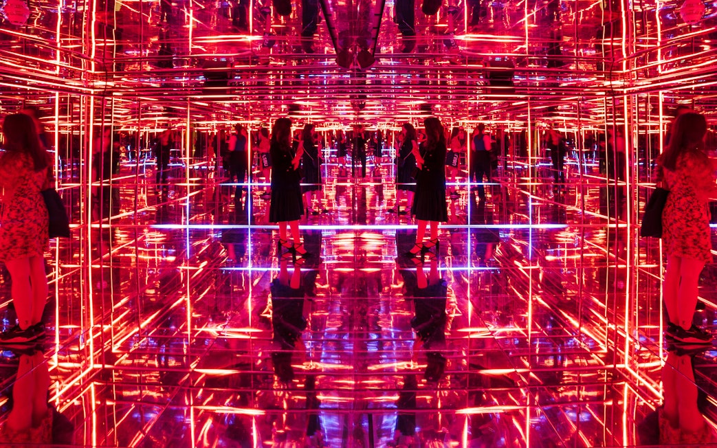 Visitors exploring neon-lit mirrored room at Moco Museum London interactive exhibit.