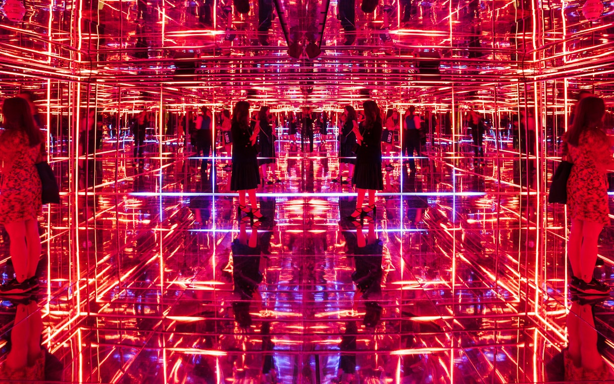 Visitors exploring neon-lit mirrored room at Moco Museum London interactive exhibit.