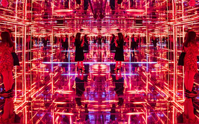 Visitors exploring neon-lit mirrored room at Moco Museum London interactive exhibit.