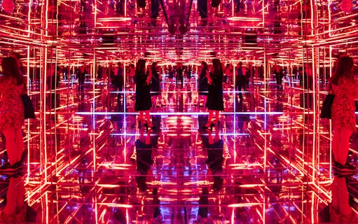 Visitors exploring neon-lit mirrored room at Moco Museum London interactive exhibit.