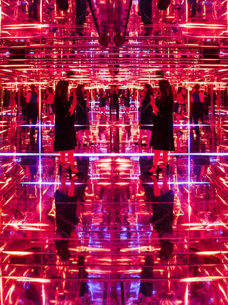 Visitors exploring neon-lit mirrored room at Moco Museum London interactive exhibit.