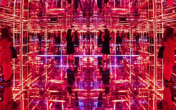 Visitors exploring neon-lit mirrored room at Moco Museum London interactive exhibit.