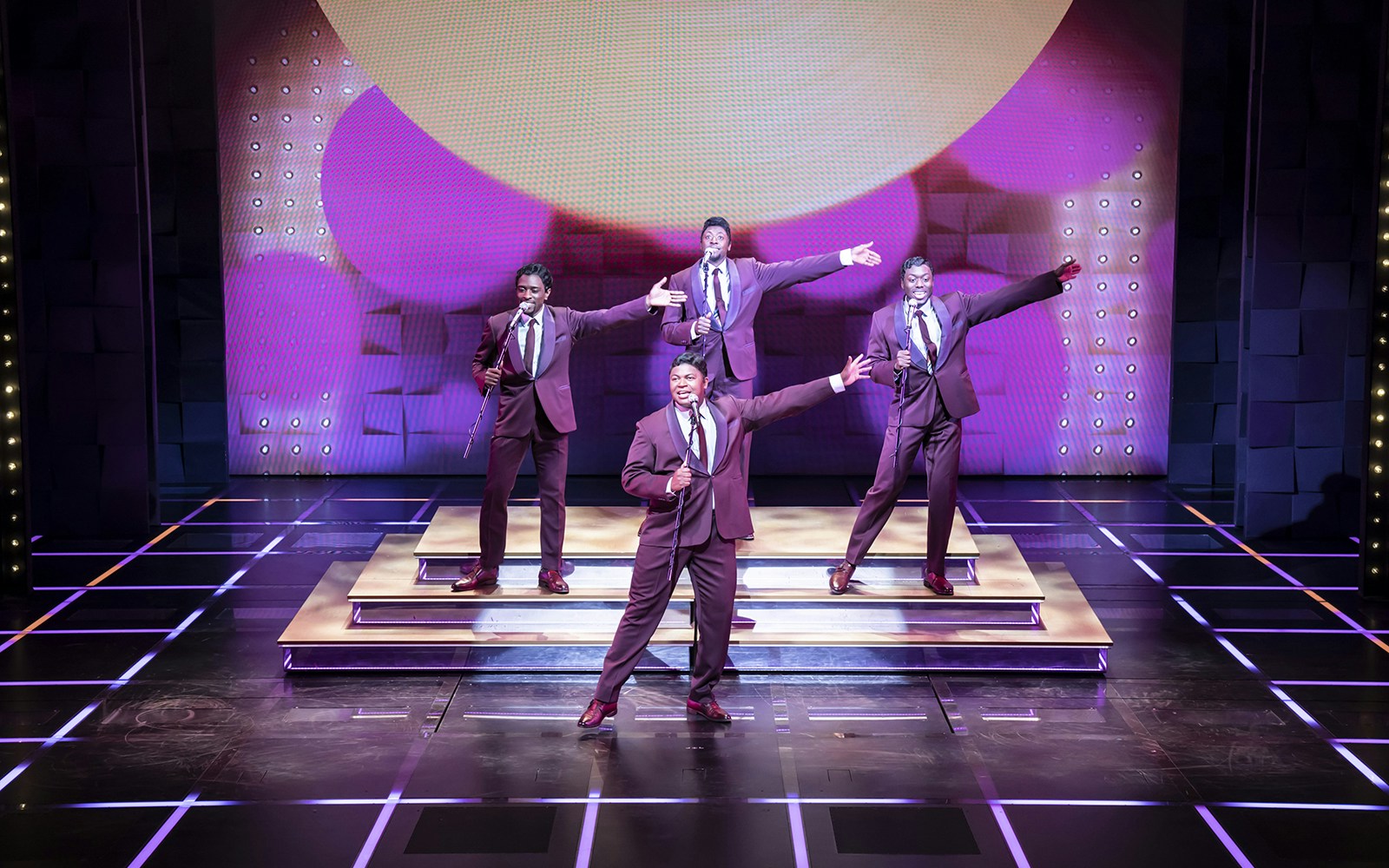 Performers on stage during "The Drifters Girl" musical, singing and dancing in suits.