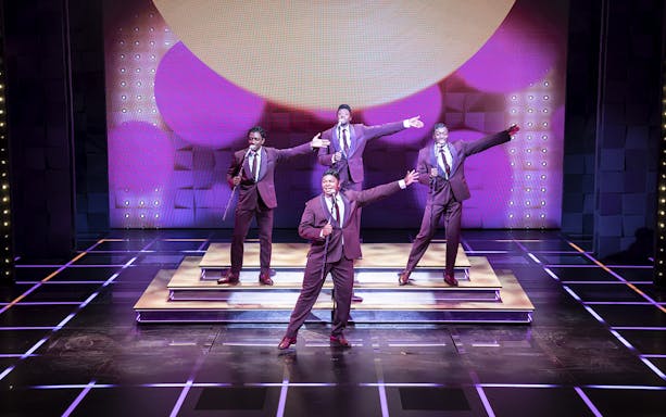 Performers on stage during "The Drifters Girl" musical, singing and dancing in suits.