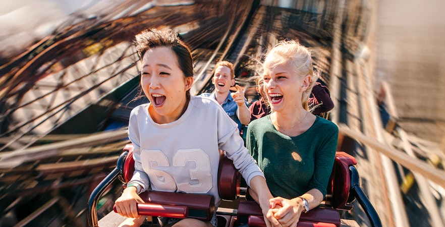 People enjoying a thrilling roller coaster ride, holding hands and smiling.