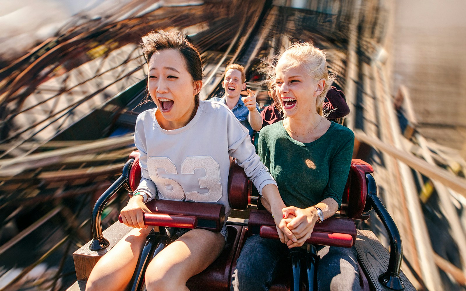 People enjoying a thrilling roller coaster ride, holding hands and smiling.