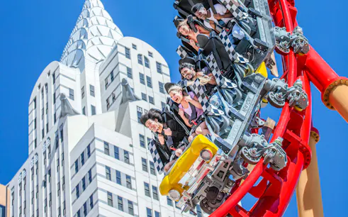 Riders on The Big Apple Coaster in Las Vegas with skyscraper backdrop.