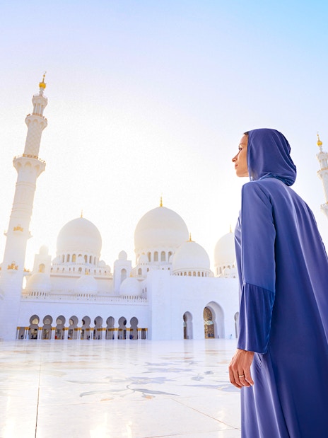 Woman in abaya at Sheikh Zayed Grand Mosque, Abu Dhabi, with domes and minarets in view.