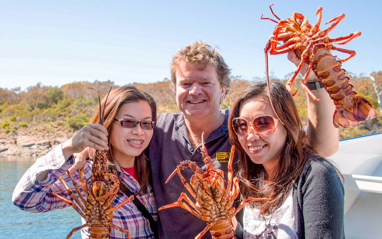 Tourists holding fresh lobsters on a Tasmanian Seafood Seduction tour.