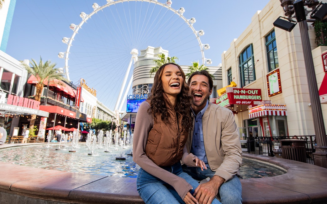 Couple smiling by fountains at The LINQ Promenade with High Roller in Las Vegas.