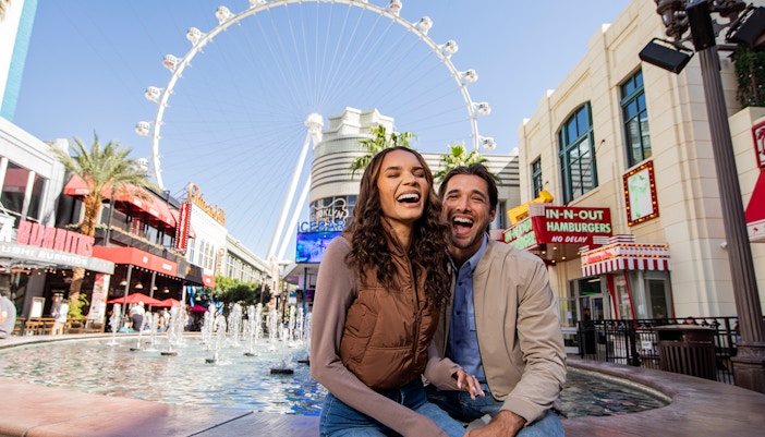Couple smiling by fountains at The LINQ Promenade with High Roller in Las Vegas.
