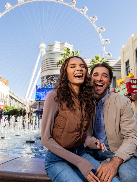 Couple smiling by fountains at The LINQ Promenade with High Roller in Las Vegas.