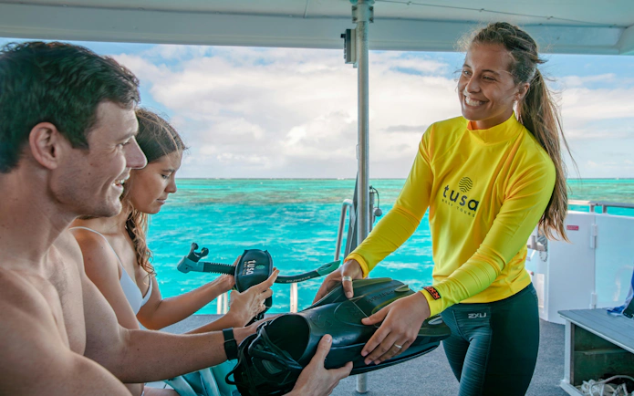 Snorkeling guide handing equipment to tourists on a boat near Cairns.