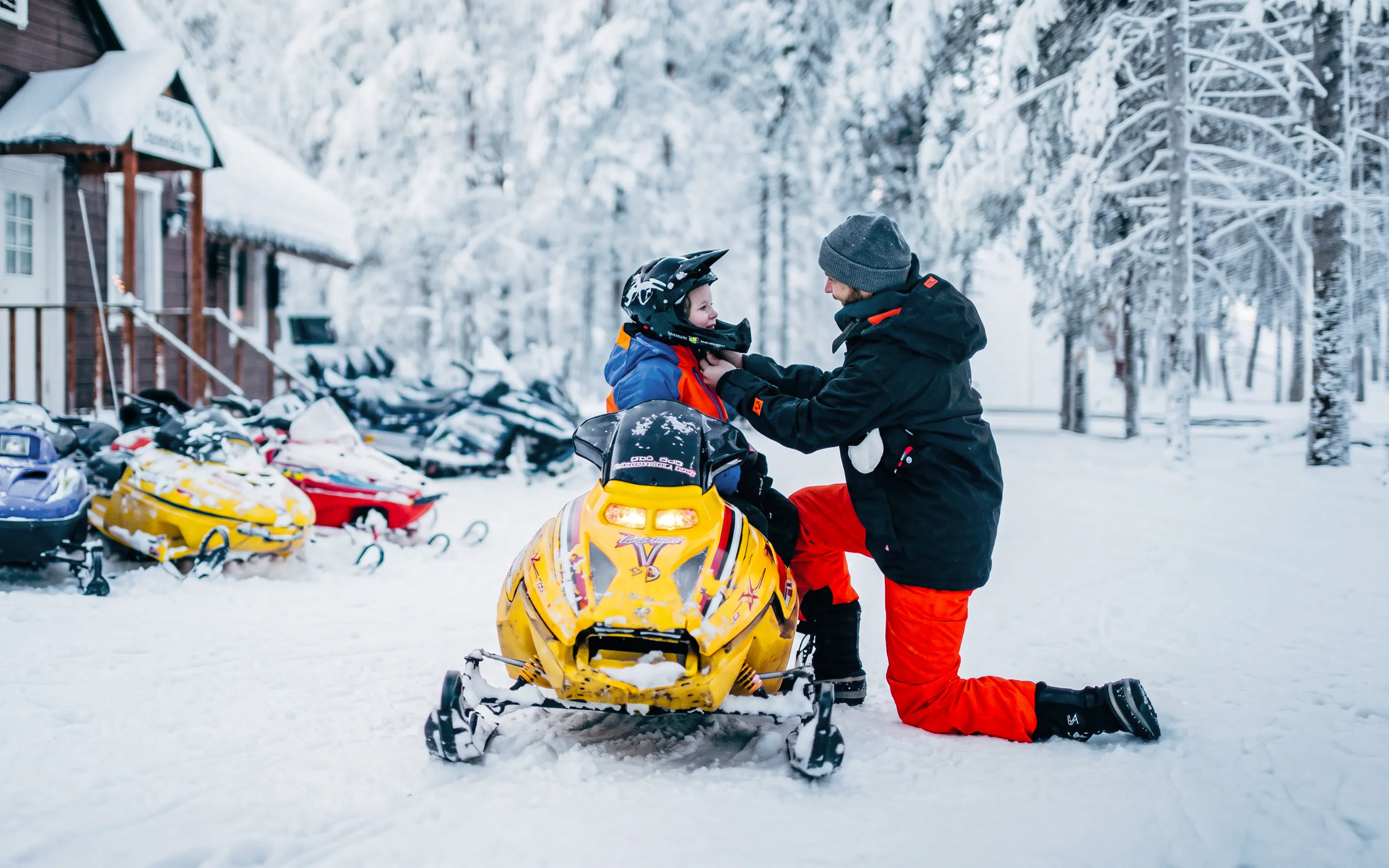 Man adjusting child's helmet on snowmobile at Arctic Circle Snowmobile Park, Finland.