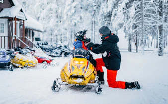 Man adjusting child's helmet on snowmobile at Arctic Circle Snowmobile Park, Finland.