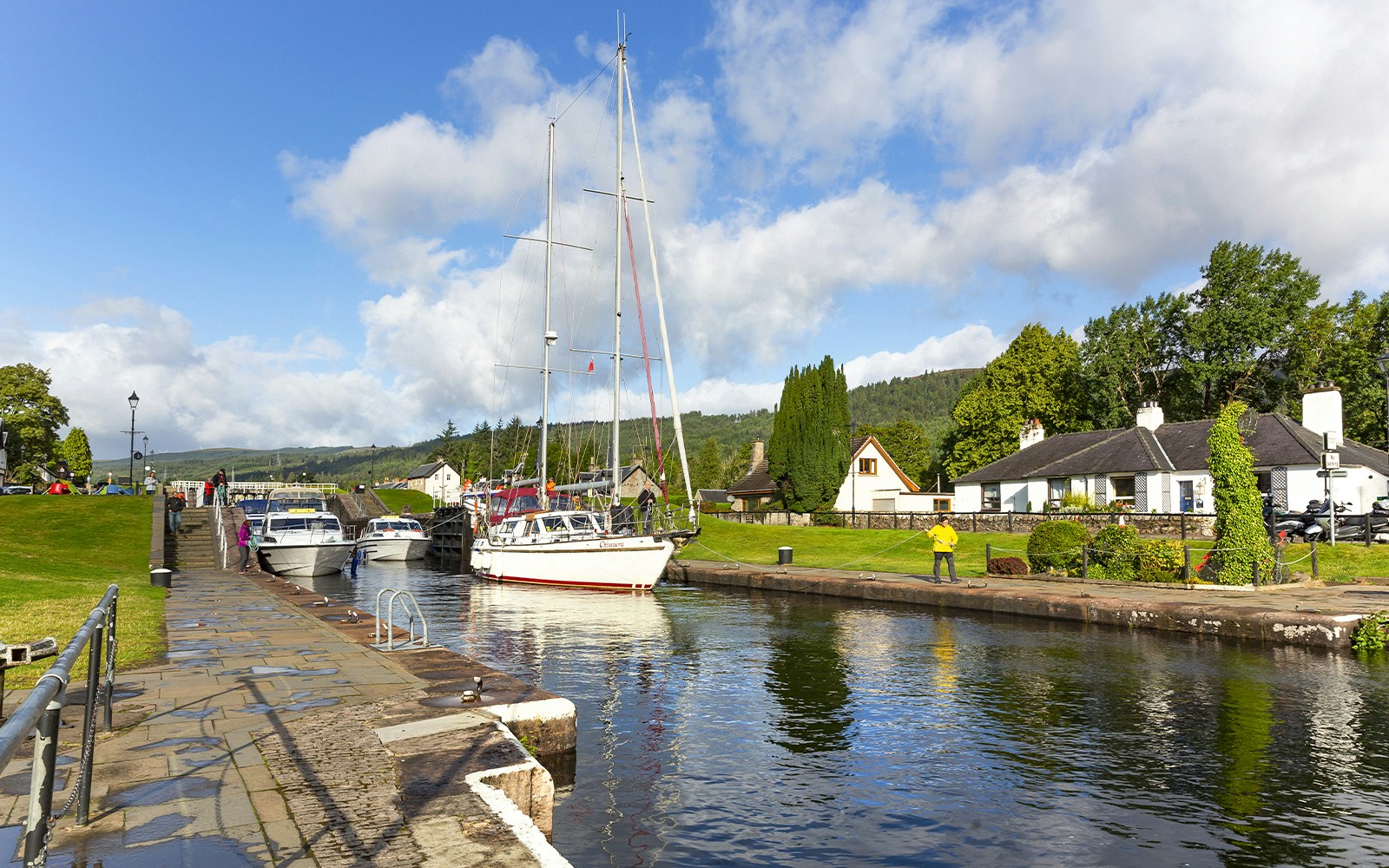 Boats docked at a canal in Loch Ness with the scenic Highlands in the background on a tour from Inverness.