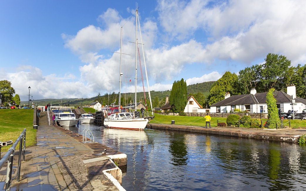 Boats docked at a canal in Loch Ness with the scenic Highlands in the background on a tour from Inverness.