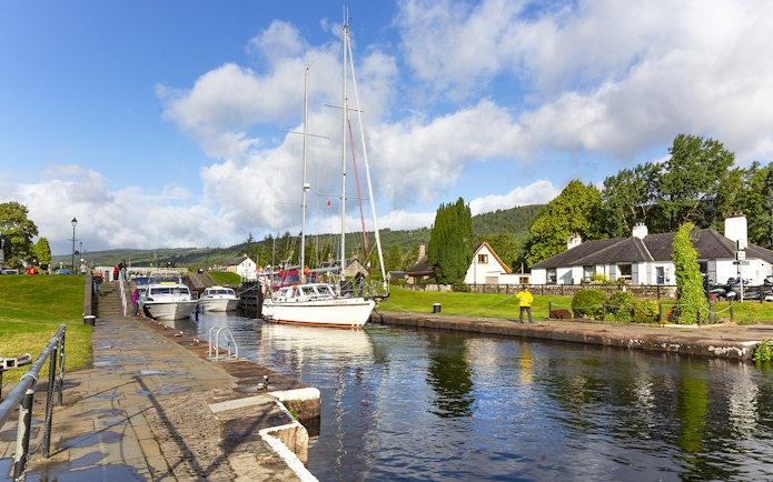 Boats docked at a canal in Loch Ness with the scenic Highlands in the background on a tour from Inverness.