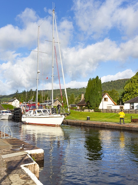 Boats docked at a canal in Loch Ness with the scenic Highlands in the background on a tour from Inverness.
