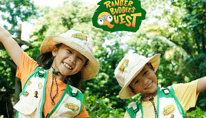 Children smiling in Ranger Buddies hats and vests, surrounded by lush greenery.