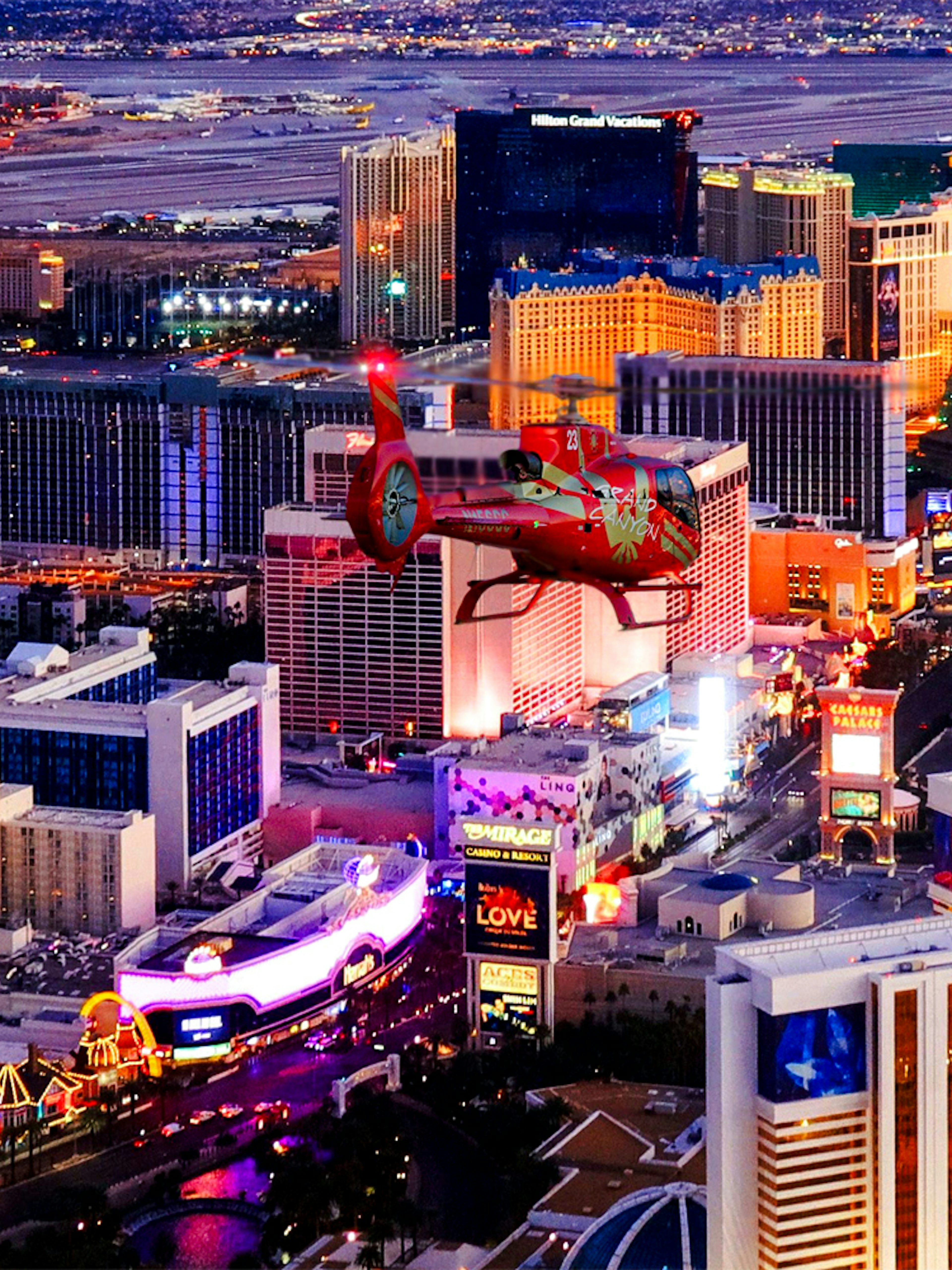 Aerial view of the illuminated Las Vegas Strip at night with a helicopter in the foreground.