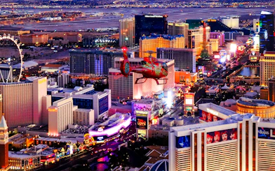 Aerial view of the illuminated Las Vegas Strip at night with a helicopter in the foreground.