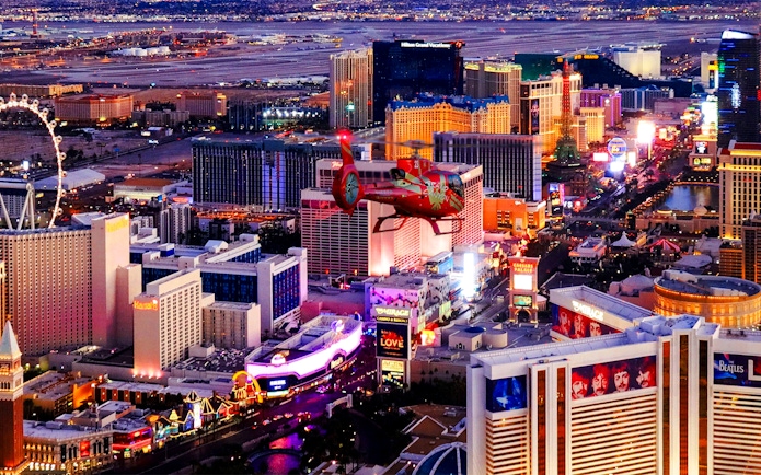 Aerial view of the illuminated Las Vegas Strip at night with a helicopter in the foreground.