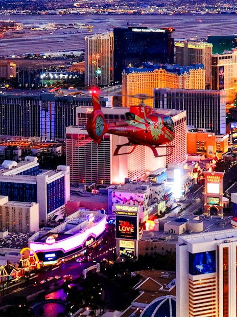 Aerial view of the illuminated Las Vegas Strip at night with a helicopter in the foreground.