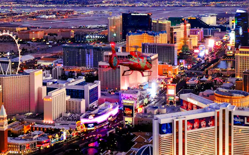 Aerial view of the illuminated Las Vegas Strip at night with a helicopter in the foreground.
