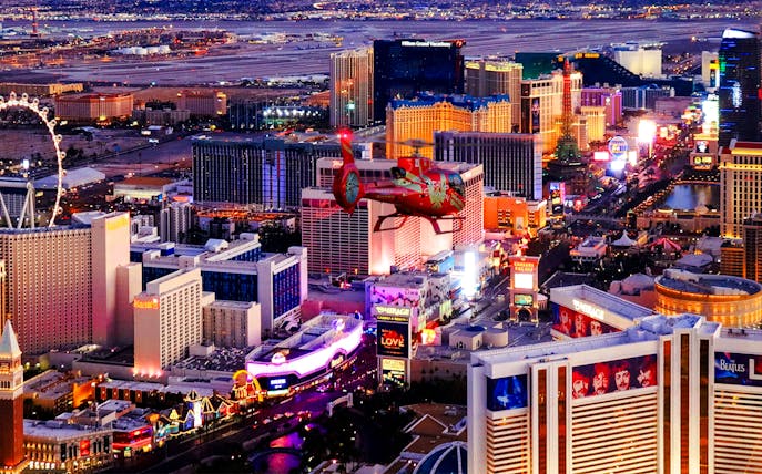 Aerial view of the illuminated Las Vegas Strip at night with a helicopter in the foreground.
