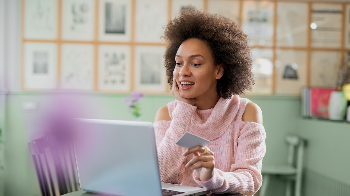 Une femme tenant sa carte bancaire devant son ordinateur portable