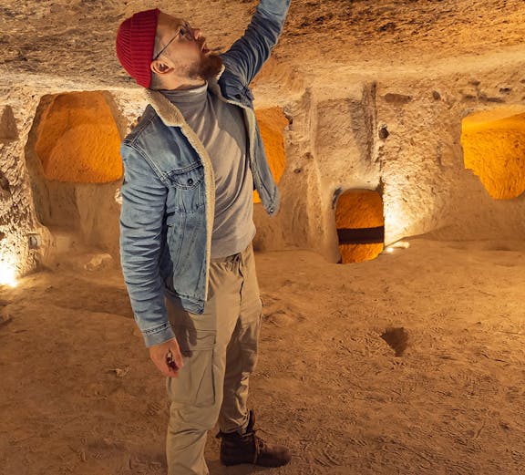 Visitor exploring Kaymakli Underground City, examining ancient stone ceiling.