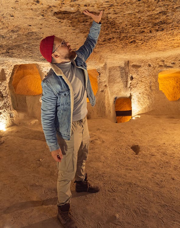 Visitor exploring Kaymakli Underground City, examining ancient stone ceiling.