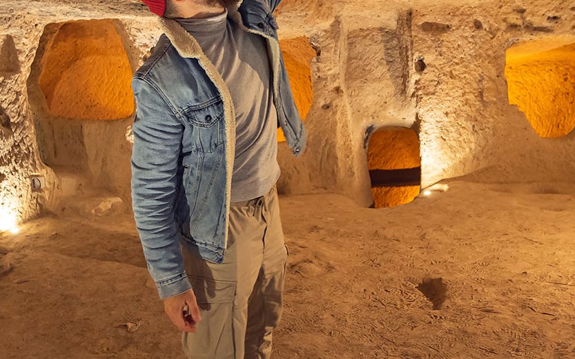 Visitor exploring Kaymakli Underground City, examining ancient stone ceiling.
