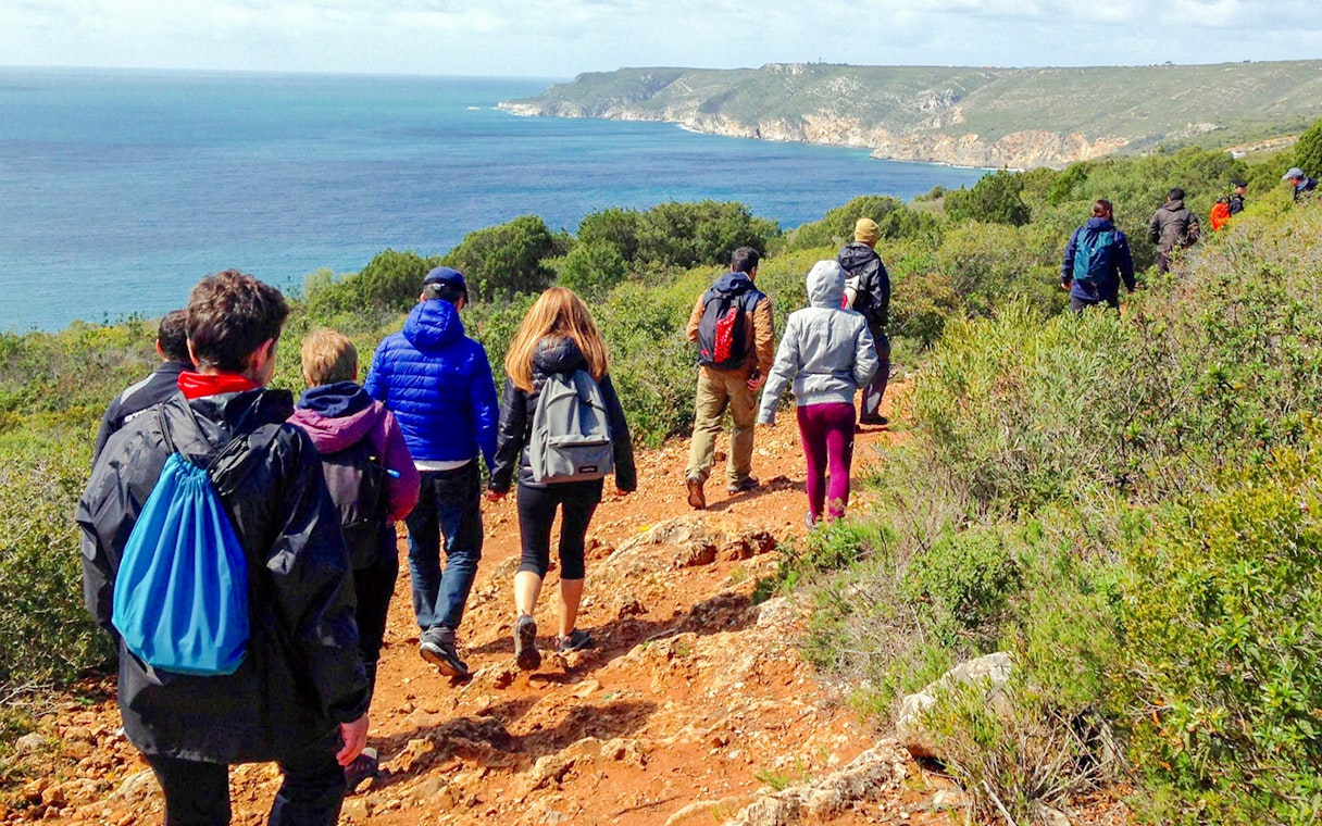 Group hiking along a trail with ocean views at Arrábida Natural Park.