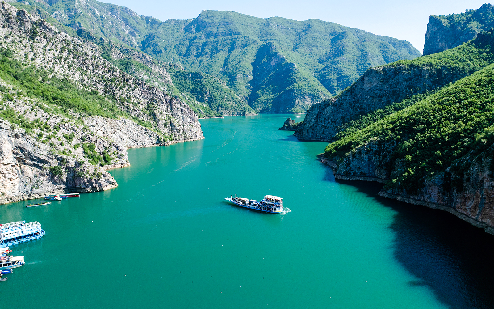 Aerial view of Komani Lake with boat navigating between mountains in Shkoder, northern Albania.