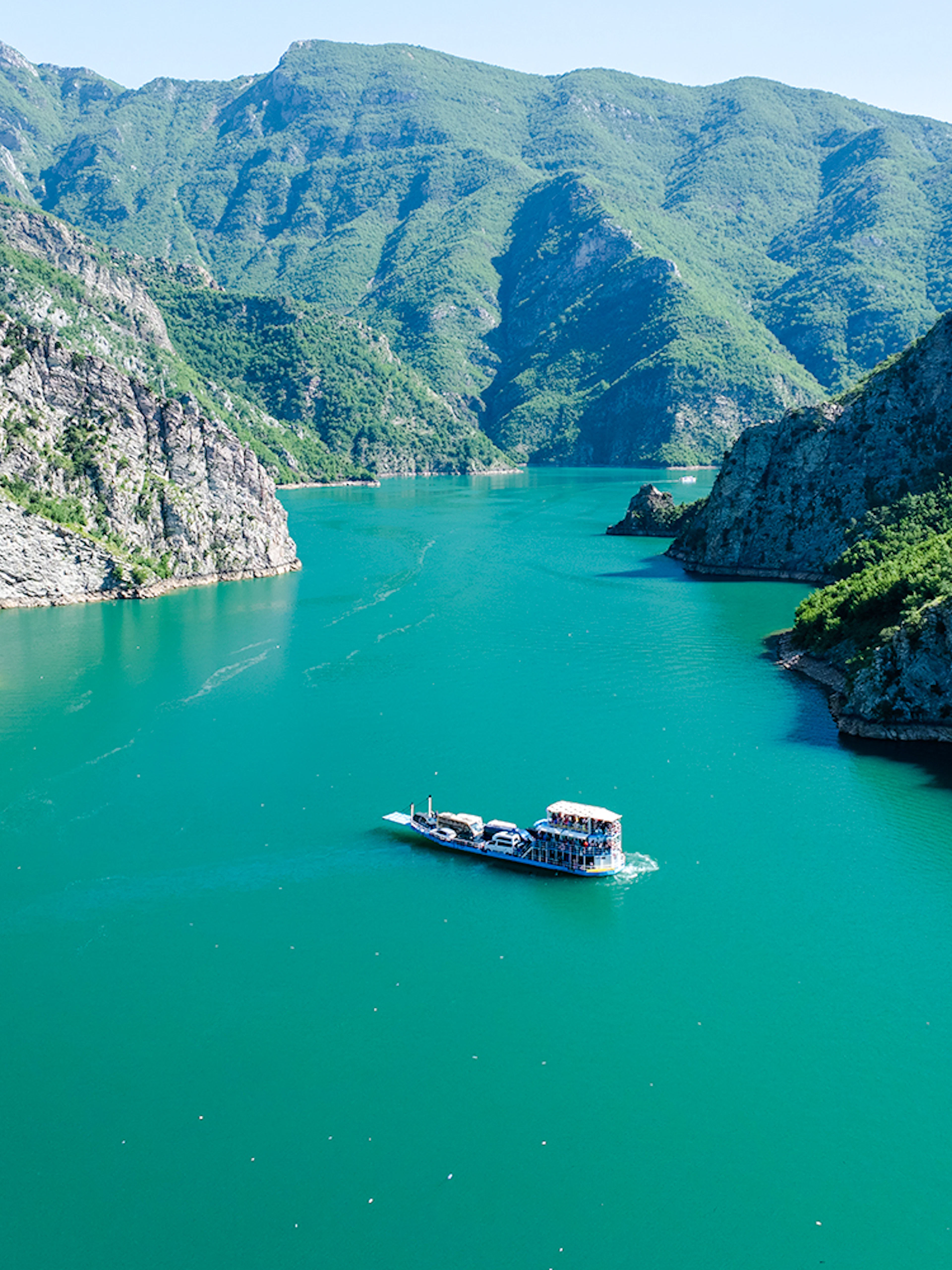 Aerial view of Komani Lake with boat navigating between mountains in Shkoder, northern Albania.