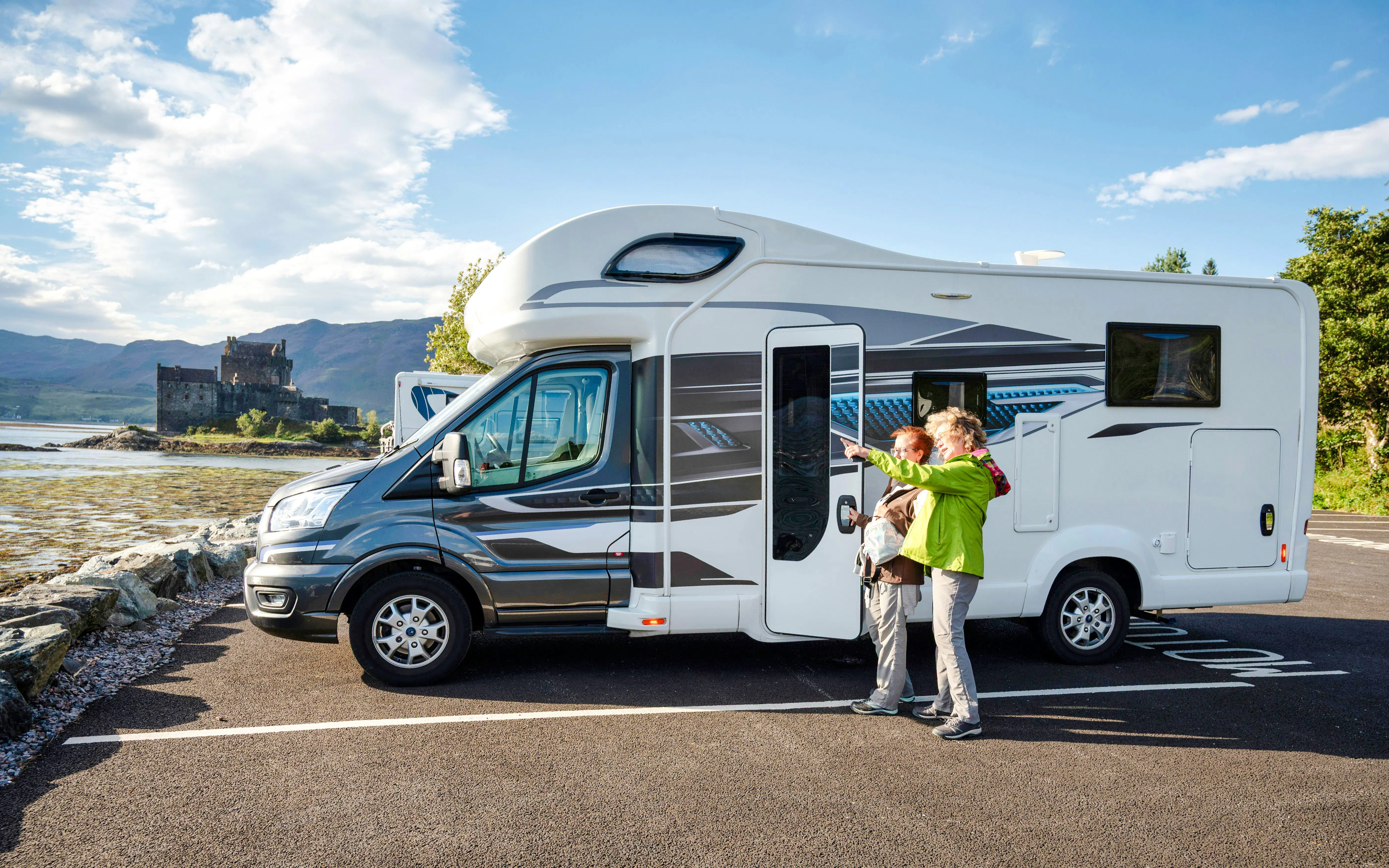 couple exploring Scottish Highlands in motorhome parked near scenic Eilean Donan Castle by the loch 