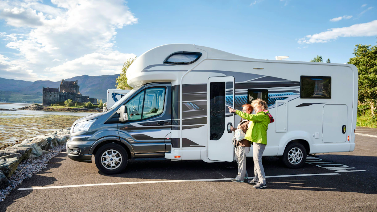 couple exploring Scottish Highlands in motorhome parked near scenic Eilean Donan Castle by the loch