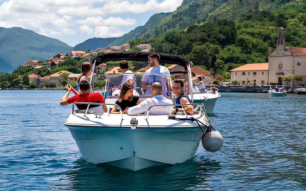 Guests on a speedboat tour near Blue Caves, with coastal village and mountains in the background.