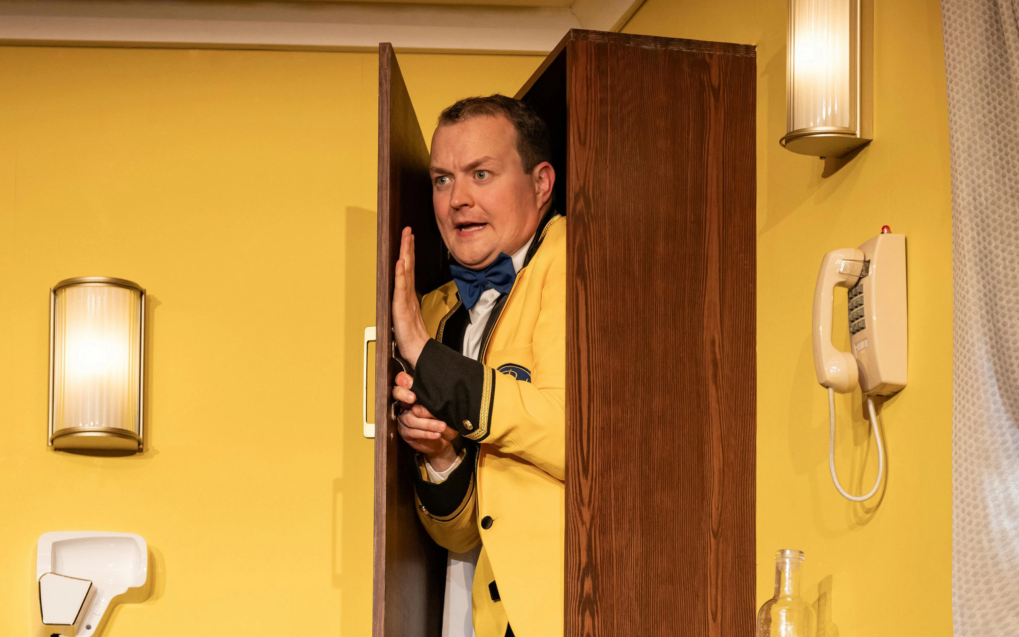 Performer in yellow jacket hiding behind door in "The Comedy About Spies" show.