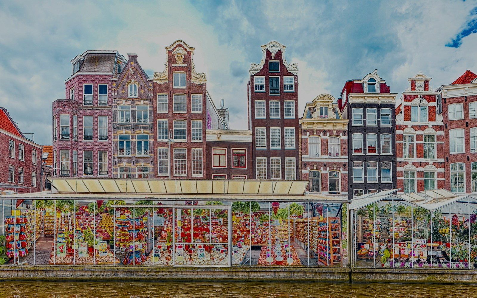Flower market stalls along the canal with traditional Dutch buildings in Amsterdam.