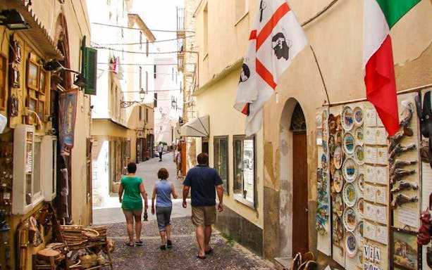 Tourists walking through a narrow street in Alghero's historic center, Sardinia.