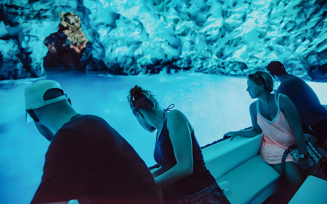 Tourists on a boat inside the illuminated Blue Cave during Blue Lagoon and 5 Islands tour.